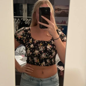 Blommig croppad topp - Säljer en superfin blommig croppad topp med korta ärmar. Perfekt för sommardagar eller en festkväll. Den har en söt, elastisk passform som sitter bekvämt. Den är endast använd nån enstaka gång och är därför i väldigt fint skick, köparen står för frakten💖