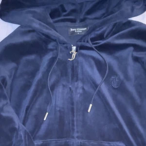 Mörkblå hoodie från Juicy Couture - Säljer en supermjuk och snygg mörkblå hoodie från Juicy Couture. Den har en dragkedja med ett coolt J-hänge och broderad logga på bröstet. Perfekt för en chill dag eller en avslappnad utekväll. 🧥✨ I färgen Blue depths, perfekt skick. Nypris: 1300kr, säljer för: 750kr