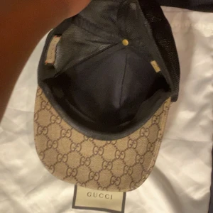 Gucci keps med tigertryck - Säljer en snygg Gucci keps med det klassiska GG-mönstret och coola tigertryck på framsidan. Kepsen har en beige bas med svarta detaljer och är perfekt för att ge din outfit en lyxig touch. Passar både till vardags och fest!