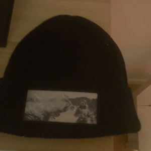 Svart mössa med tryck - Säljer en svart mössa med ett coolt tryck framtill. Perfekt för att hålla sig varm och stilren under de kallare månaderna. Mössan är i bra skick och passar de flesta huvudstorlekar. Ett måste för vintern! 🖤pris kan diskuteras