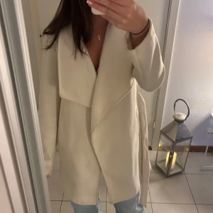 Kräm vit kappa med knytband - Säljer en stilren kräm vit kappa med knytband i midjan. Perfekt för höst och vår, med en elegant och tidlös design. Den har långa ärmar och en mjuk, bekväm passform. Passar både till vardags och festliga tillfällen. 💕 Nypris 599!!