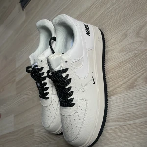 Nike Air Force 1 i vitt med svarta detaljer - Speciell designade snören. Helt oanvända. Pris kan diskuteras!