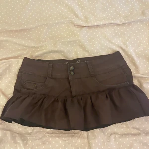 Brun minikjol med volang - RESERVERAD, KÖP EJ ‼️Säljer en superfin brun kortkjol med volangdetaljer. Kjolen har en klassisk jeansstil med knappar fram och fickor både fram och bak. står ingen storlek men skulle säga att det är en S
