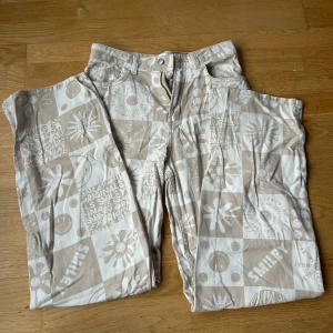 Beige mönstrade byxor H&M - Säljer ett par unika beige och vita byxor från H&M med coolt mönster av smileys och blommor. De har dragkedja och knapp framtill. Använda 2 gånger så i toppen skick 🤍 jag är 165 cm. 100 % bomull