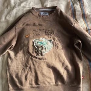 Brun sweatshirt från Nike - Säljer en brun sweatshirt från nike i bra skick. Den har ett coolt tryck med texten 'Runner Gear' och en broderad logga på framsidan. Tröjan är perfekt för höst och vår, med långa ärmar och ribbade muddar. Skön och stilren för vardagsbruk!