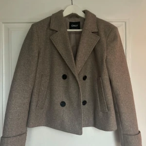 Beige kappa från ONLY - Säljer en snygg beige kappa från ONLY i storlek S. Den har en klassisk dubbelknäppt design med svarta knappar och långa ärmar. Perfekt för höst och vår, och funkar både till vardags och fest. Kappan är i mycket bra skick, knappt använd och ger en stilren look. Nypris 749 :-