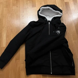 Svart Jacka från Moose Knuckles - Säljer en svart jacka/hoodie från Moose Knuckles i storlek XL. Jag personligen har L och den passar mig bra och kan skicka måtten om det behövs. Den har en mysig vit foder som går att ta bort så det blir en hoodie och dragkedja framtill. Perfekt för kyliga dagar. Huvan har snörning för justering. Pris kan diskuteras!