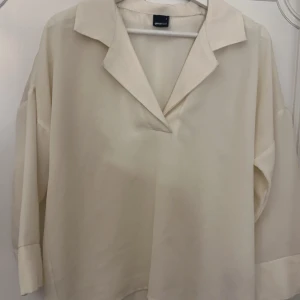 Beige blus från Selected Femme - Säljer en stilren vit blus från Gina Tricot. Den har en avslappnad passform med trekvartsärmar och en klassisk krage. Perfekt för både vardag och festliga tillfällen. Materialet känns mjukt och skönt mot huden. Passar bra till både jeans och kjol!