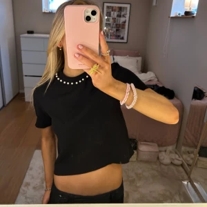 Svart croppad topp med pärldetaljer - Säljer en snygg svart croppad topp med pärlor längs halsringningen. Toppen har korta ärmar och är perfekt för en stilren och chic look. Passar både till vardags och festliga tillfällen. 🖤