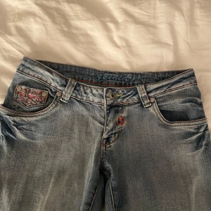 Blå jeans med broderi - Säljer ett par jätte snygga blå jeans från ZINNIA i storlek 38.De är lågmidjade och bootcut och har ett coolt broderi på bak och ena framfickan i rosa och orange med små stenar,en liten lapp där bak med blommor i rött,rosa,grönt,gult,lila,orange för att vara noga,har även lite broderi runt gylfen.Framfickorna är igensydda som man ser på bilden så man kan inte lägga nått i de. Köpte de här på plick men de var tyvärr för stora. Innerbenslängd:71cm Midjemått:35cm platt   Skriv om ni har frågor❤️