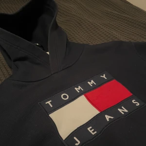 Mörkblå hoodie från Tommy Jeans - Säljer en snygg mörkblå hoodie från Tommy Jeans med deras ikoniska logga i rött, vitt och blått på bröstet. Perfekt för en casual look och superbekväm med känguruficka framtill. Passar perfekt till höst och vinter! ❗️Kom med prisförslag❗️