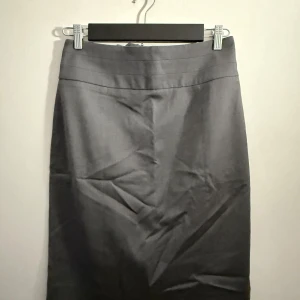 Grå kjol från H&M - Snygg grå pennkjol från H&M i storlek 40. Kjolen har en stilren design med en diskret dragkedja bak. Perfekt för både kontoret och vardagsbruk. Materialet känns bekvämt och har en fin passform. Ett måste i garderoben för en klassisk look!
