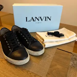 Säljer ett par snygga svarta sneakers från Lanvin i skinn. De har en klassisk design med snörning och en vit sula som ger en stilren look. Perfekta för både vardag och fest! Skorna kommer med originalkartong och dustbag.