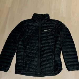Svart dunjacka från Peak Performance - Säljer en svart dunjacka från Peak Performance i mycket bra skick. Jackan har en dragkedja framtill och är perfekt för kyliga dagar. Den är långärmad och har en stilren design som passar både till vardags och utomhusaktiviteter. Perfekt för höst och vinter! Stor i storlek, passar 155-165👍👍 Nypris: 1599kr  Skriv vid frågor! 