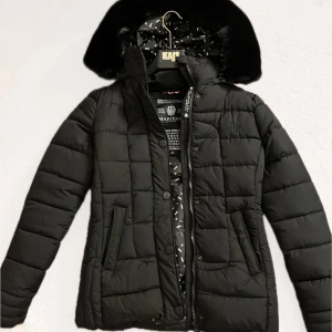 Svart vinterjacka från Marikoo - Säljer en snygg svart vinterjacka från Marikoo i mycket bra skick. Jackan har en mysig huva med pälsdetaljer och stängs med både dragkedja och knappar. Perfekt för kalla vinterdagar! 🖤