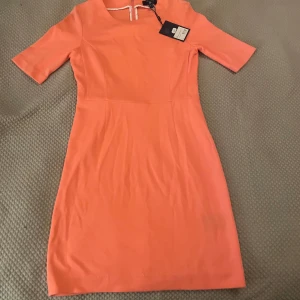 Korallfärgad klänning från GANT - Säljer en superfin korallfärgad klänning från GANT i storlek XS. Klänningen har en elegant och enkel design med korta ärmar och en dragkedja i ryggen. Perfekt för vår och sommar! Har aldrig använt.