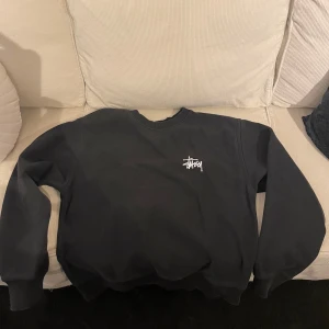 Svart sweatshirt från Stüssy - Säljer en svart sweatshirt från Stüssy i storlek S. Den har en stor vit logga på framsidan och är gjord i ett mjukt material. Perfekt för en avslappnad stil och passar bra till både jeans och joggers. Tröjan är i bra skick och redo för nya äventyr!