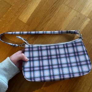 Axelremsväska  - Cool väska i rosa lila rutigt material. Är i mycket bra skick! ❤️ köparen står för frakten 
