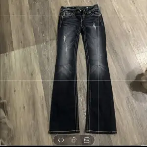 Säljer ett par snygga mörkblå bootcut jeans från Miss Me i storlek 26. De har coola slitningar och snygga broderade detaljer med pärlor på bakfickorna. Perfekta för en avslappnad men stilren look. Passar både till vardags och fest!