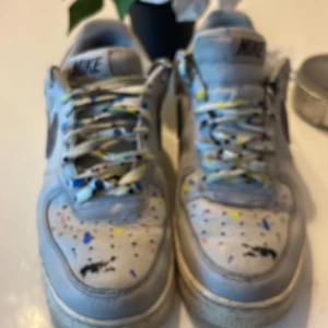 Nike sneakers med färgstänk - Säljer ett par unika Nike sneakers med coola färgstänk i blått, gult och svart. Skorna har en klassisk design med snörning och är i bra skick. Perfekta för en avslappnad stil med en twist!