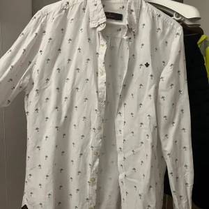 Vit skjorta med palmmönster från Morris - Säljer en snygg vit skjorta från Morris med små palmmönster. Skjortan har långa ärmar och knappar framtill. Perfekt för en avslappnad sommarlook eller en stilren vårdag. Den är i bra skick och redo för nya äventyr! 🌴