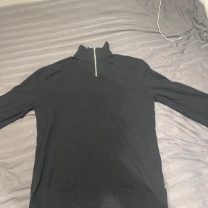 Svart tröja med dragkedja från Jack & Jones - Säljer en stilren svart tröja från Jack & Jones i storlek M. Tröjan har en praktisk dragkedja vid halsen och är perfekt för både vardag och lite kyligare dagar. Den är i mycket bra skick och passar till det mesta i garderoben. Perfekt för höst och vinter!