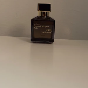 Parfym Maison Francis Kurkdjian Oud Satin Mood - Säljer en lyxig parfymflaska från Maison Francis Kurkdjian. Flaskan är elegant med en mörk ton och har en stilren svart och guld kork. Doften är Oud Satin Mood, perfekt för speciella tillfällen. En riktig klassiker för den som älskar exklusiva dofter.