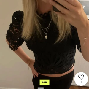 Svart spetsblus - Snygg svart spetsblus med korta ärmar och ett vackert mönster. Perfekt för en utekväll eller fest. Blusen är croppad och har en elegant design som passar både till jeans och kjol.