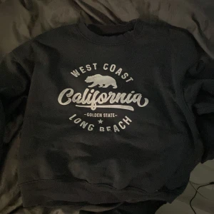 Grå sweatshirt från Bik Bok - Säljer en grå sweatshirt från Bik Bok i storlek XS. Den har ett tryck med texten 'West Coast California Long Beach' och en björn på framsidan. Perfekt för en avslappnad stil eller mysiga dagar hemma. Superbekväm och lätt att matcha med jeans eller leggings!