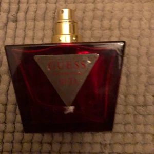 Guess Red parfym - Säljer en elegant parfym från Guess i en djup röd flaska med en triangulär etikett. 