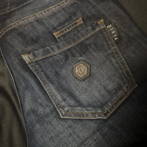 Philipp Plein jeans - Snygga Philipp Plein jeans i mörkblå denim med coola detaljer som en unik knappdesign och logotyp på bakfickan. Tillverkade i Turkiet med en blandning av bomull och polyester för en bekväm passform. Perfekta för både vardag och fest!