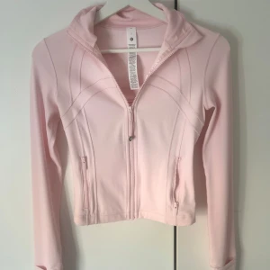Ljusrosa jacka från Lululemon - Säljer en superfin ljusrosa jacka från Lululemon i storlek 2. Den har en dragkedja framtill och två praktiska fickor med dragkedjor. Perfekt för vår och höst, eller när du vill ha en lätt jacka för träning. Materialet är mjukt och stretchigt, vilket gör den bekväm att bära. Endast änvand två gånger så i jätte bra skick💕💕👌🏻Cropped version!!