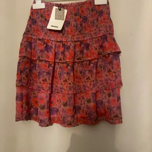 Blommig kjol från Bik Bok - Superfin blommig kjol från Bik Bok i härliga färger som rosa, lila och röd. Kjolen har en volangdetalj och är perfekt för sommaren. Den är kort och har en elastisk midja för en bekväm passform. Perfekt för både vardag och fest!