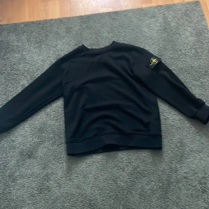 Svart tröja från Stone Island. - Säljer en svart tröja från Stone Island i mycket bra skick. Den har en klassisk design med långärmade ärmar och det ikoniska märket på ärmen. Perfekt för både vardag och lite mer avslappnade tillfällen. Passar bra till höst och vinter. Den passar även M eller S 