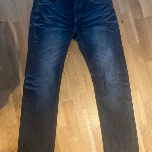Mörkblå jeans med unik look - Säljer ett par mörkblå jeans i bra skick. De har en klassisk straight passform. Jeansen har en snygg wash med lätt slitna detaljer. Mått finns på bilderna.