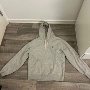 Grå hoodie från Polo Ralph Lauren - Säljer en grå hoodie från Polo Ralph Lauren i bra skick. Den har en liten logga på bröstet och en klassisk känguruficka. Perfekt för höst och vår! Det finns en liten fläck på framsidan, men annars är den i fint skick. Skön och stilren för vardagsbruk. Storlek M men sitter lite mindre än M.