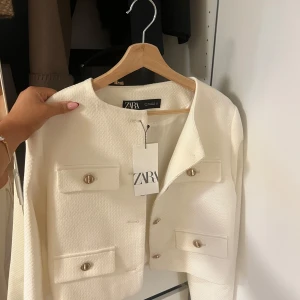 Vit kavaj från Zara - Säljer en stilren vit kavaj från Zara har aldrig använt den. Den har en elegant design med knappar framtill och två fickor med lock. Perfekt för både vardag och fest😍