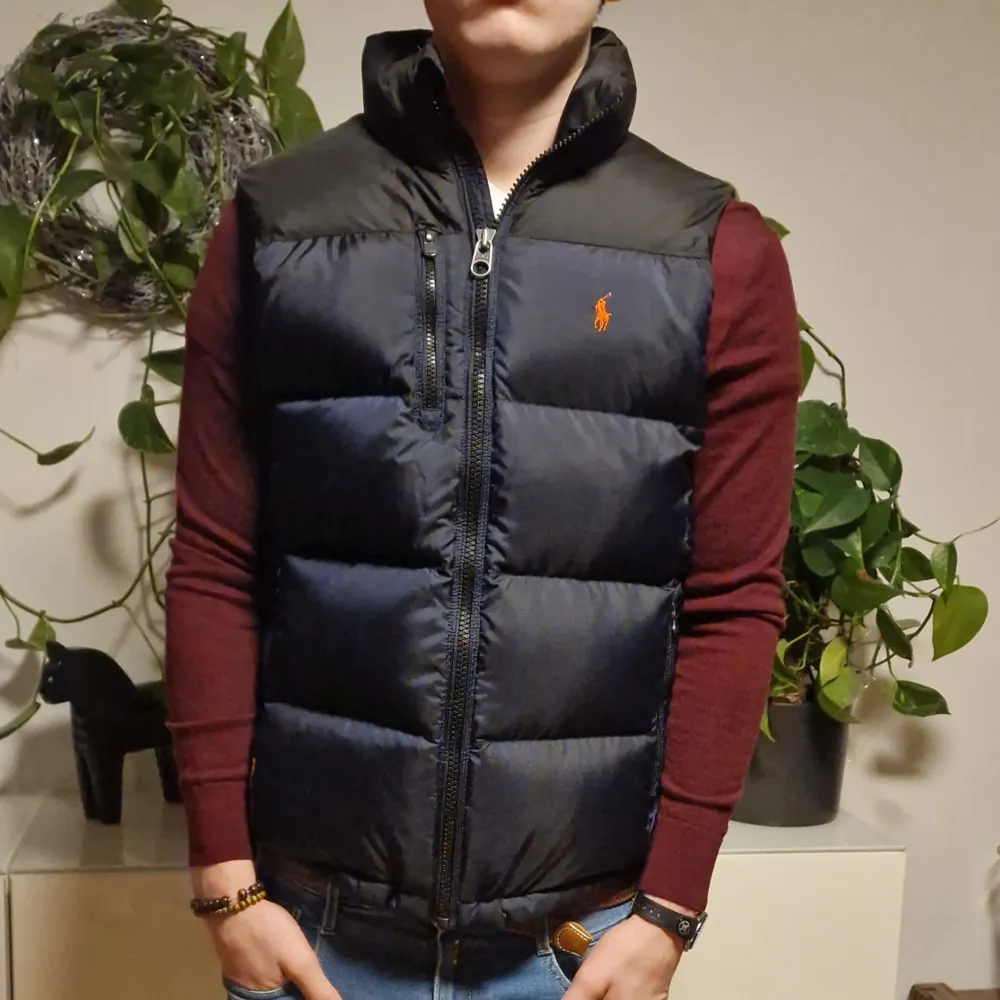 Ursnygg blå/svart, mycket varm puffer dunväst i toppskick, storlek M.  Orange logga på bröstet. Perfekt julklapp att ge bort och att hålla värmen med stil!                       Modellen är 181 cm lång och väger 74 kg, så passar dom med storlek S och M oxå.. Jackor.