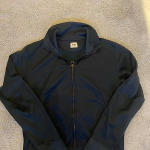 Mörkblå tröja från Acne - Säljer en stilren mörkblå tröja från Acne i storlek L. Tröjan har en dragkedja framtill och en hög krage, perfekt för kyliga dagar. Den är i mycket bra skick och passar både till vardags och lite finare tillfällen. Skön och enkel att matcha med andra plagg!