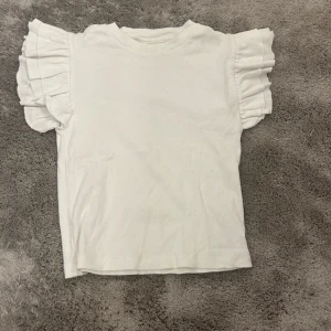 Fyra toppar i olika stilar - Säljer fyra olika toppar. En vit ribbad topp med volangärmar, perfekt för sommaren. En enkel vit croppad t-shirt, lätt att matcha. En svart t-shirt i normal passform, ett basplagg i garderoben. Slutligen en svart topp med spetsdetaljer och puffärmar, idealisk för festliga tillfällen. Den första tröjan är i storlek 146/152. Andra tröjan är i storlek 152. Näst sista tröjan är i storlek 150. Sista tröjan är i storlek 146/152. Alla tröjor använda fåtal gånger.🤍🥰