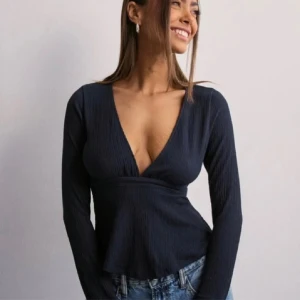 Mörk blå topp från Nelly  - Säljer en snygg blå  topp med v-ringning. Den har långa ärmar och en figursydd passform som ger en smickrande siluett. Perfekt för både vardag och fest! Säljer eftersom den sitter lite kort på mig (jag är 172) men den är i bra skick utan några skador