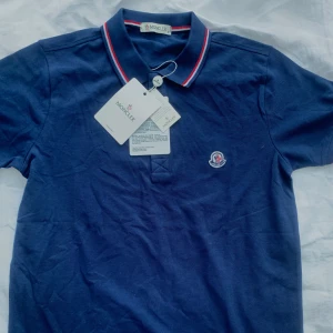 Mörkblå pikétröja från Moncler - Säljer en snygg mörkblå pikétröja från Moncler i nytt skick. Piquen kommer med Kvitto och allt är splitter nytt. Kan gå me i pris vid snabb affär. Nypris:3000kr