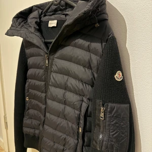 Svart quiltad jacka från Moncler - Säljer en snygg svart quiltad jacka från Moncler i mycket bra skick. Jackan har långa ärmar och en dragkedja framtill. Den är perfekt för höst och vinter med sitt stilrena och varma design. Passar både till vardags och lite finare tillfällen.  Köpt från moncler hemsida, kvittens online, är i ett bra skick utan några skador, säljer pågrund av att den börjar bli liten, 7-10 månader gammal