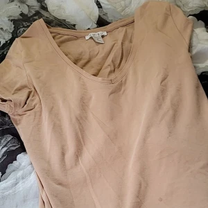 Beige kortärmad topp från Amisu - Säljer en enkel och stilren beige topp från Amisu. Den har en v-ringad hals och korta ärmar, perfekt för vardagsbruk eller sommarens varma dagar. Toppen är i ett mjukt och bekvämt material.