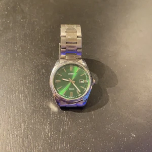 Casio herrklocka med grön urtavla - Säljer en snygg Casio herrklocka i mycket bra skick. Den har en grön urtavla med silverdetaljer och datumvisning. Armbandet är i rostfritt stål och ger en stilren look. Perfekt för både vardag och fest! Storleken är oklar. Om du har stor handleder så tänk över innan köp. Klockan har några repor osv men inget märkbart på håll