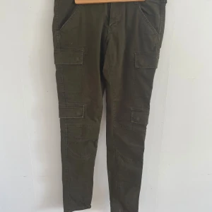 Olivgröna cargobyxor - Säljer ett par olivgröna cargobyxor i bomull. De har flera praktiska fickor på sidorna och bak, vilket ger en cool och funktionell stil. Perfekta för en avslappnad look eller utomhusaktiviteter.