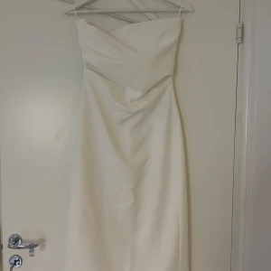 Vit klänning - Axelbandslös vit klänning i hållbart material. Liten rynkning vid midjan. Vadlång 