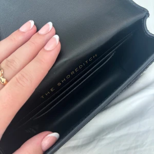 Svart glittrig axelväska från Kurt Geiger - Säljer en superfin svart axelväska från Kurt Geiger med glittriga detaljer i olika färger. Väskan har en cool kedjerem och ett snyggt spänne framtill. Perfekt för en utekväll eller fest! Säljer för 1500 köpte för 2400! Kan diskutera priset, ungefär inte använd🤗
