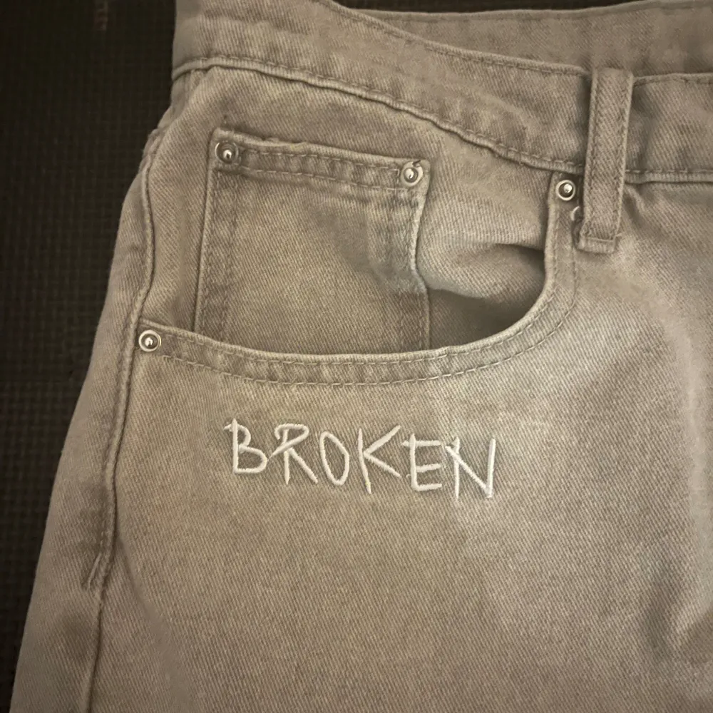 Säljer ett par grå jeans från Broken Planet Market. De har coola broderade detaljer med ordet 'BROKEN' och stjärnliknande mönster. Jeansen har en straight passform och är perfekta för en avslappnad stil. De är i storlek W32 L32 och har en klassisk femficksdesign.. Jeans & Byxor.