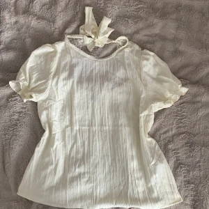 Kortärmad blus - Gullig vit kortärmad blus från SHEIN. Jätte gulliga detaljer både fram och bak, (även en rosett som man kan knyta där bak) Storlek M men är liten i storleken. Den ser mer gul ut i verkligheten. 🩶